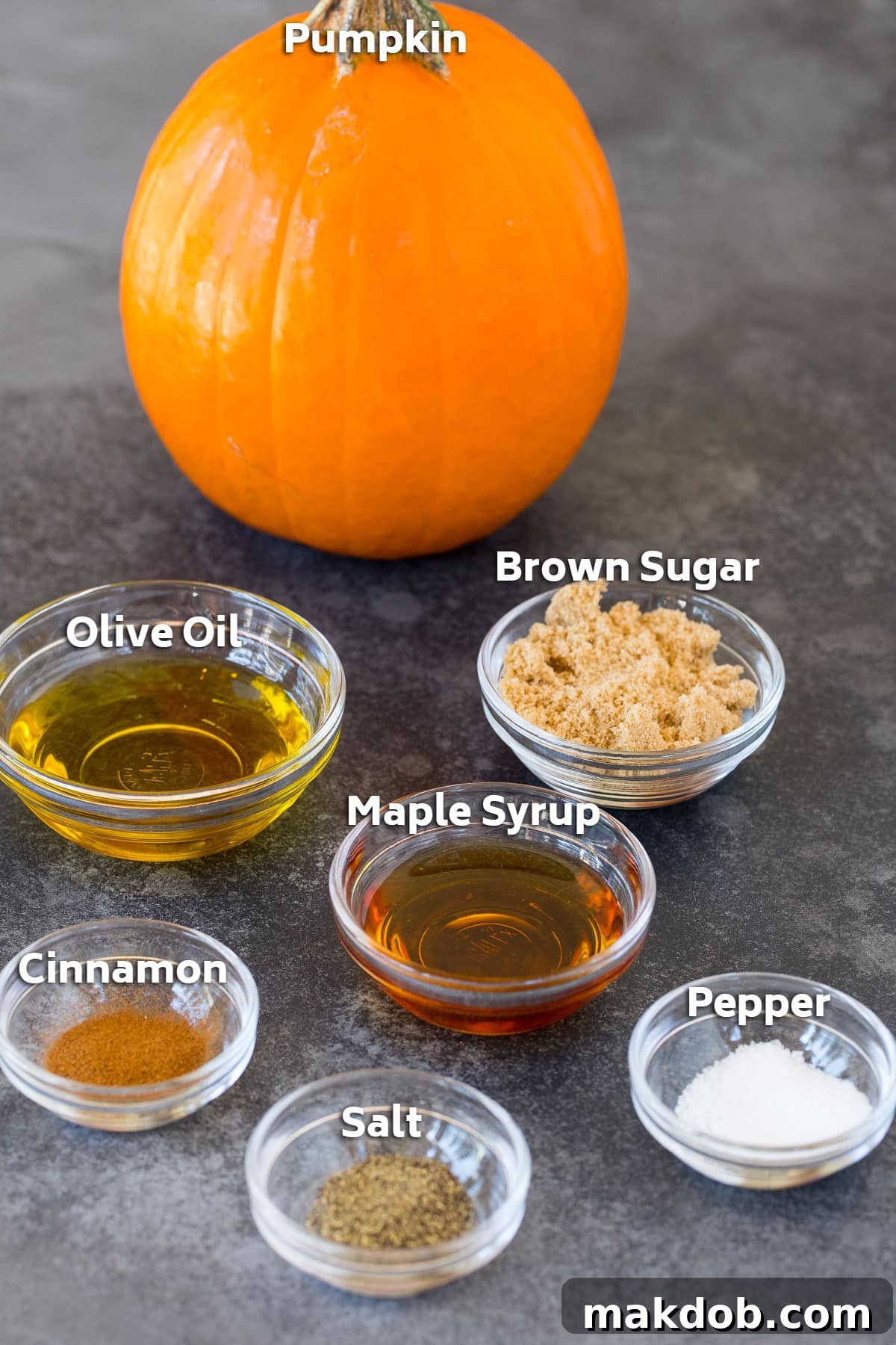 A collection of ingredients laid out, including olive oil in a cruet, brown sugar, a spice jar, and a small bowl of salt and pepper, ready for a roasted pumpkin preparation.