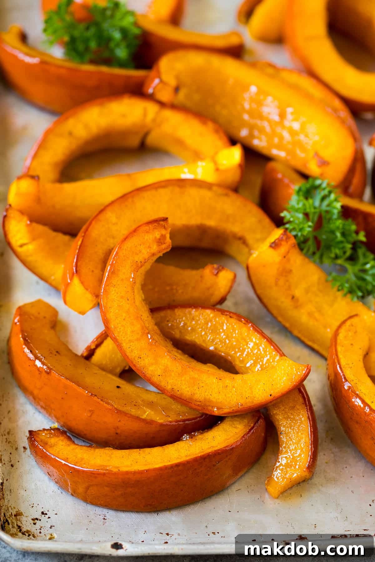 Roasted pumpkin wedges on a sheet pan, garnished with fresh parsley, ready to be served.