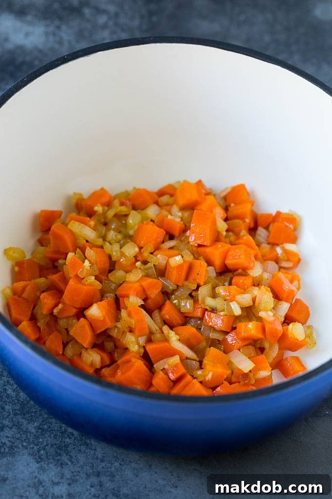 Aromatics Sautéing in a Pot Sautéed carrots, onions, and minced garlic simmering in a pot, forming the aromatic base for the rich pumpkin soup.