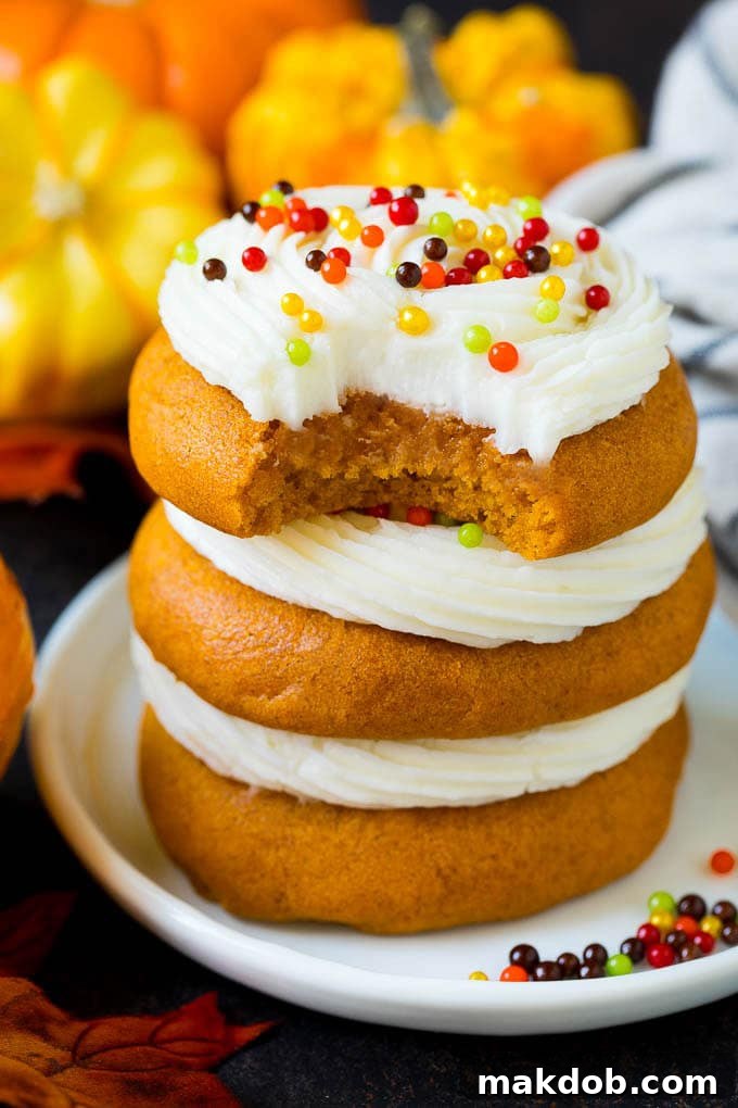 Savor the taste of fall with these beautifully frosted pumpkin cookies. A stack of soft pumpkin cookies, with one showing a bite taken out, revealing its moist interior and creamy frosting.