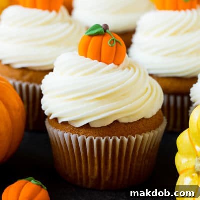 Pumpkin cupcakes topped with cream cheese frosting and candy pumpkins, presented on a white serving plate.
