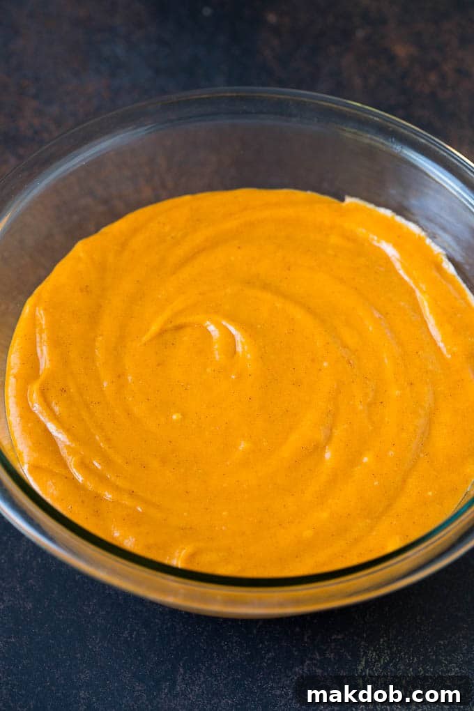 A mixing bowl filled with a smooth, amber-colored pumpkin cupcake batter.