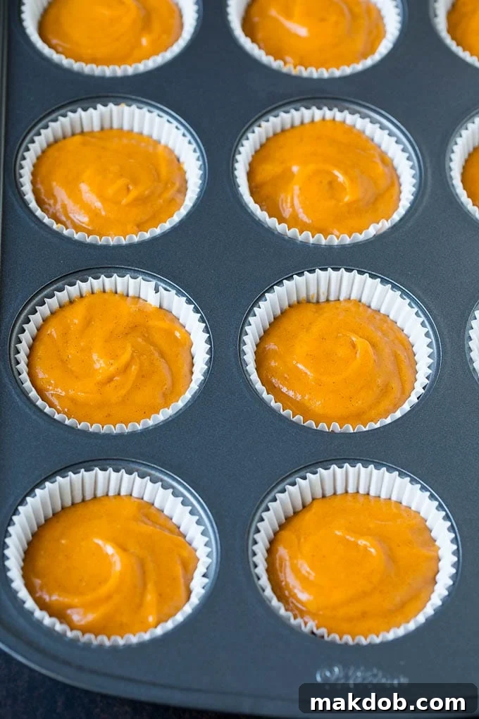 Pumpkin cupcake batter filling paper liners in a muffin tin, ready for baking.