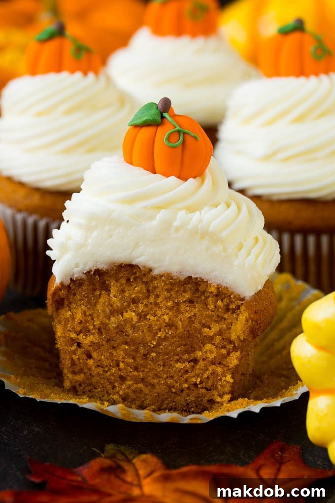 A pumpkin cupcake, sliced in half to reveal its moist interior, beautifully arranged with fall leaves and gourds.