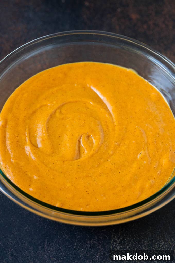 A bowl of pumpkin cake batter, light orange and smooth, ready to be poured into a baking pan.