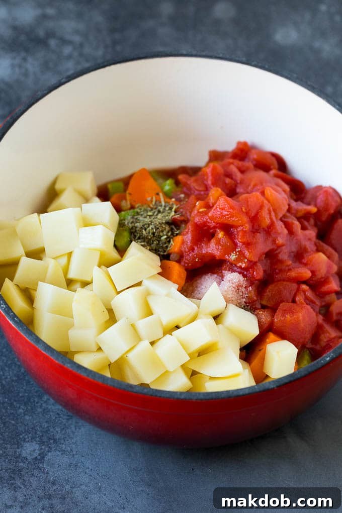 A culinary close-up showing a large pot filled with colorful vegetables, uniformly diced potatoes, and rich crushed tomatoes, all simmering in a savory broth.