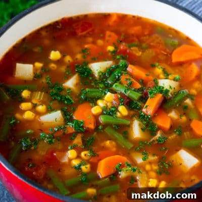 A pot of vegetable soup filled with colorful veggies, potatoes and herbs, ready to be served.
