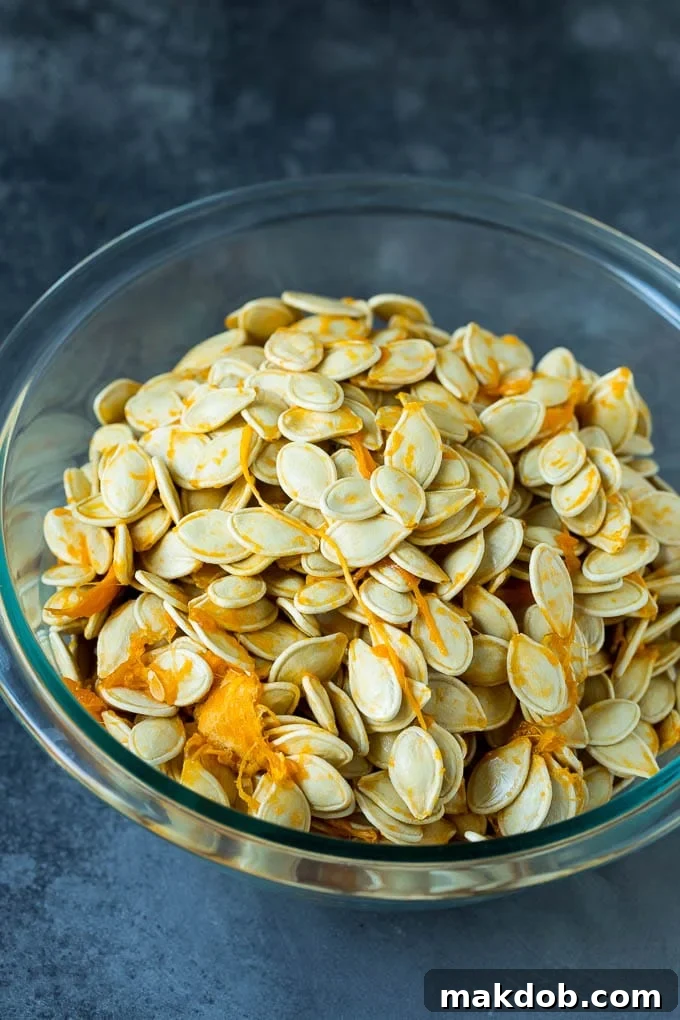 A large ceramic bowl filled with freshly scooped pumpkin seeds still attached to stringy pumpkin flesh, illustrating the initial raw state before cleaning.