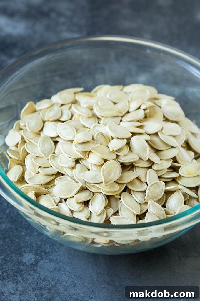 Perfectly cleaned and dried pumpkin seeds spread thinly on a sheet pan, showcasing their readiness for the next step of seasoning.