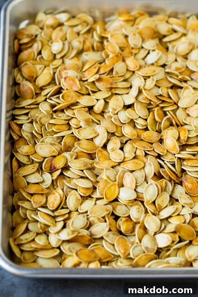 A large sheet pan generously covered with a single layer of perfectly golden-brown roasted pumpkin seeds, fresh out of the oven and looking irresistibly crunchy.