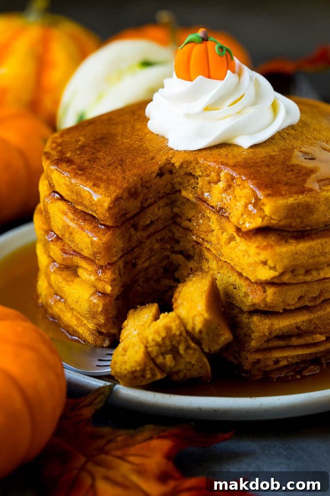 A stack of golden pumpkin pancakes, perfectly cooked and ready to eat, with a fork holding cut pieces of pancake, inviting you to take a bite.