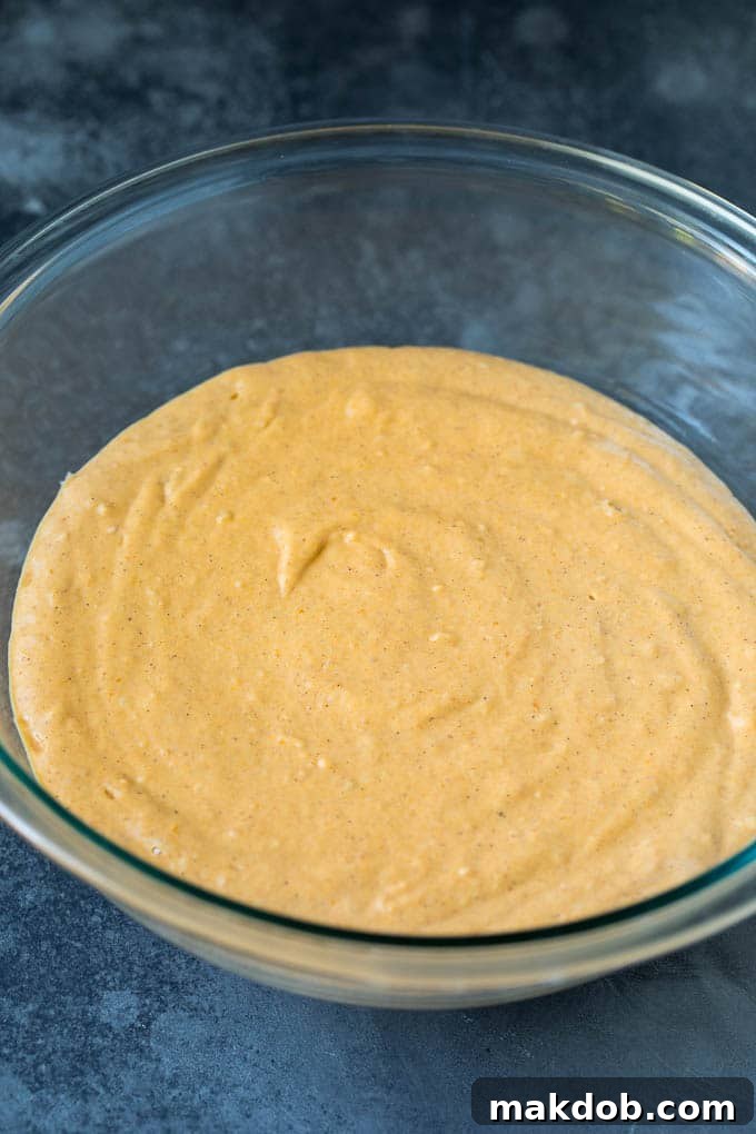 Pancake batter, enriched with pumpkin puree and spices, swirled in a mixing bowl, ready to be cooked into fluffy hotcakes.