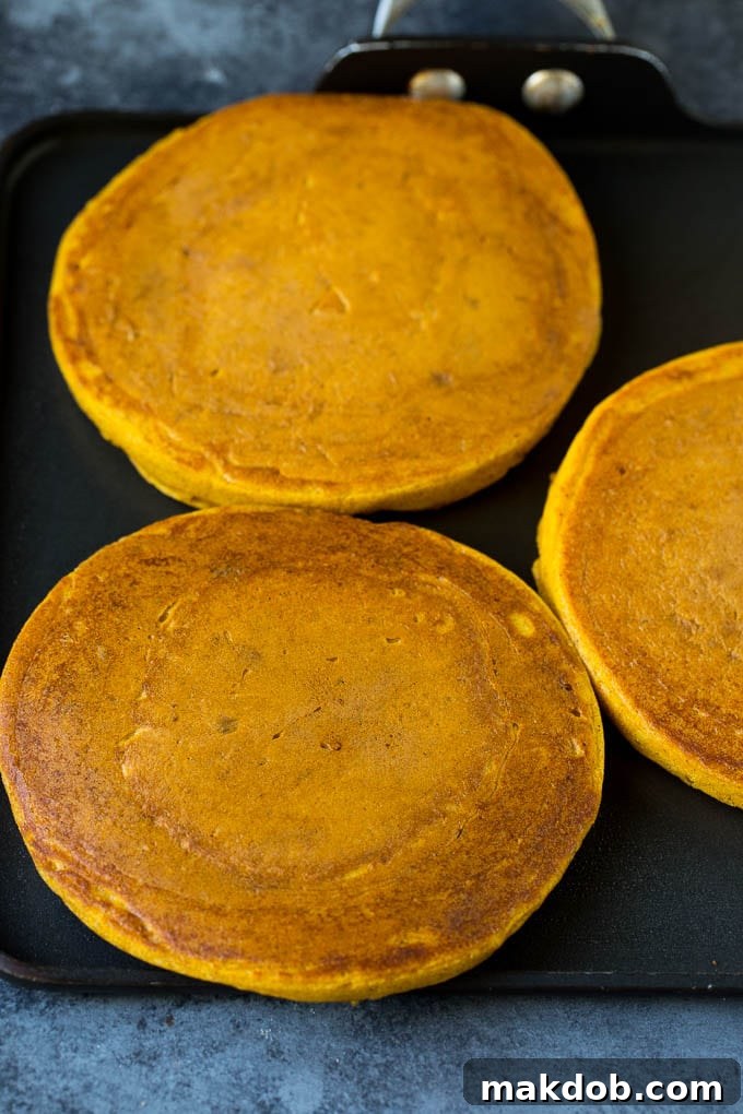 Hot pumpkin hotcakes sizzling on a griddle, their edges turning golden brown, signaling they are almost ready to flip.