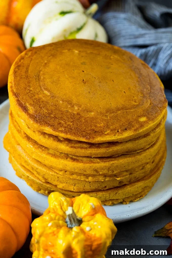 A stack of golden brown pumpkin hot cakes, surrounded by rustic fall decorations like pinecones and autumn leaves, evoking a cozy atmosphere.