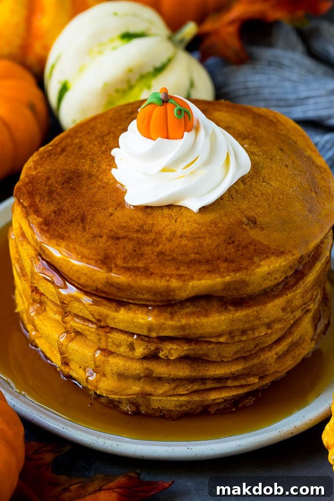 A glorious stack of pumpkin pancakes, generously topped with a cascade of pure maple syrup and a cloud of fluffy whipped cream, tempting any breakfast lover.