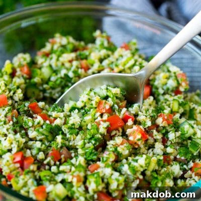 A bowl of vibrant tabbouleh salad with a serving spoon, garnished with fresh mint, ready for consumption.