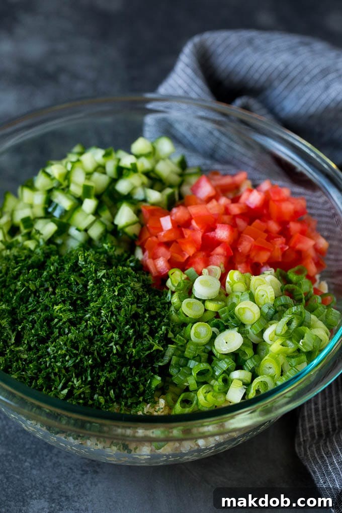 A bowl of bulgur topped with herbs, tomatoes and cucumber.