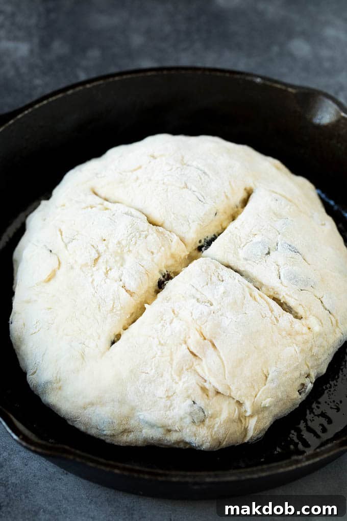 Irish Soda Bread Recipe #bread #baking #stpatricksday #sidedish #dinneratthezoo A perfectly shaped loaf of Irish soda bread, scored with an X, in a cast iron skillet ready for baking.
