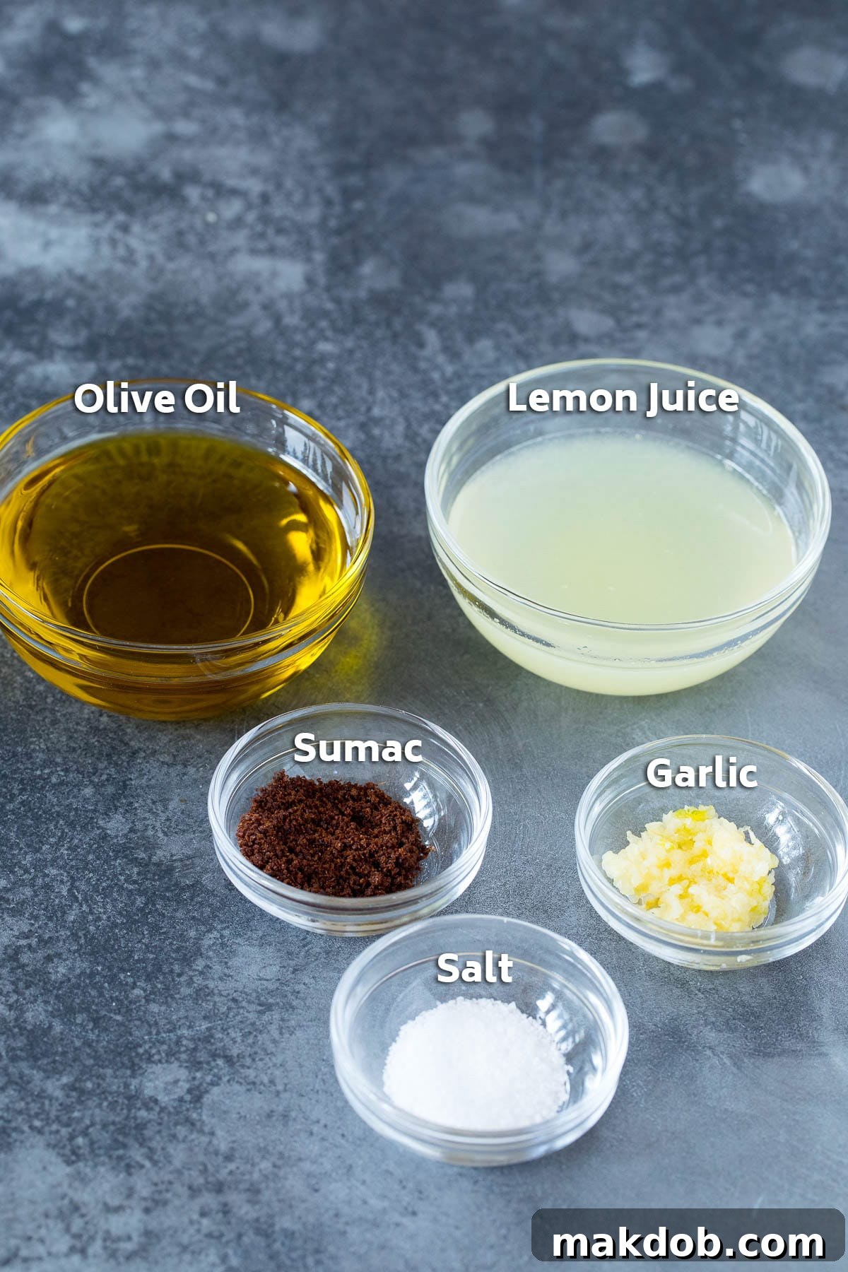 Small bowls containing olive oil, fresh lemon juice, and various seasonings, prepared for mixing into a Fattoush dressing.