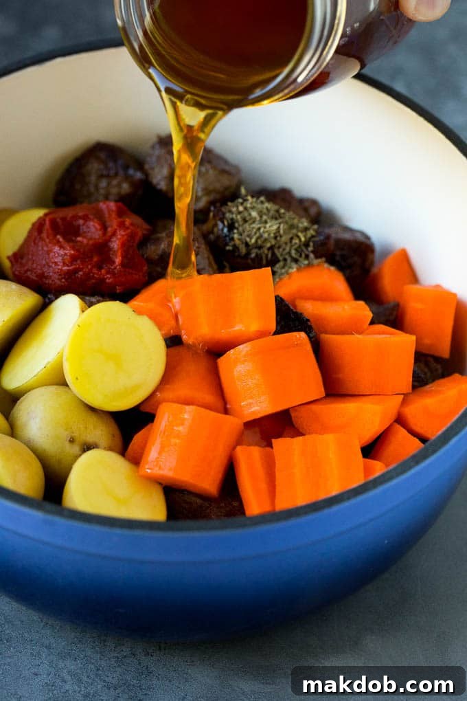 Adding Broth to Irish Stew Ingredients Pouring rich beef broth into a pot filled with seared beef, chopped carrots, and potatoes, prior to simmering for Irish stew.