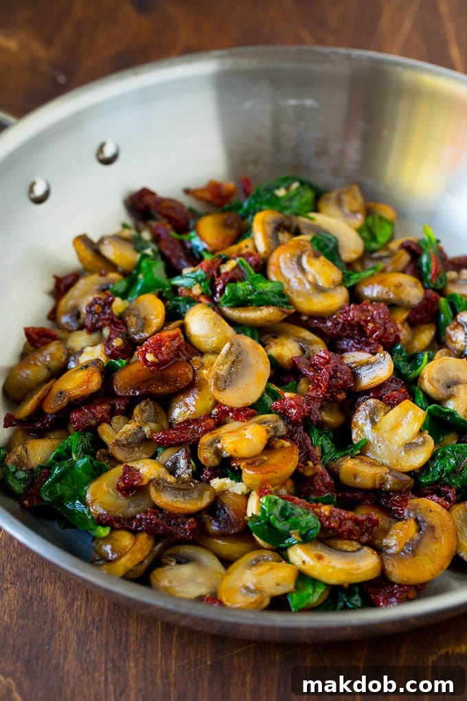 A pan filled with sauteed mushrooms, garlic, wilted spinach, and sun-dried tomatoes, ready for the sauce.