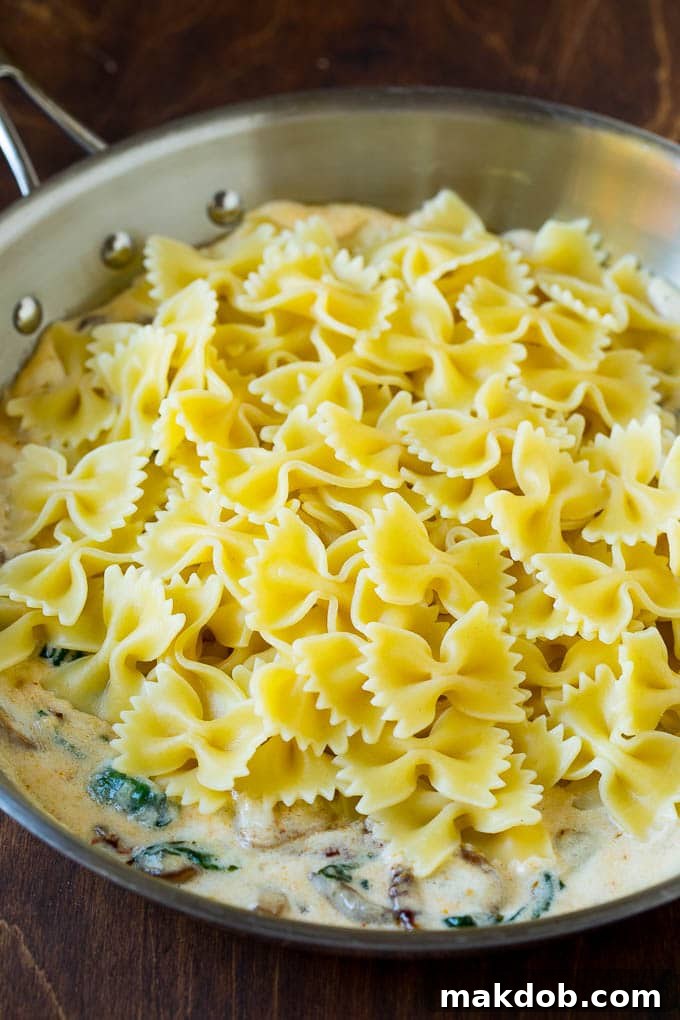 Cooked farfalle pasta being tossed in a pan of rich, creamy sauce.