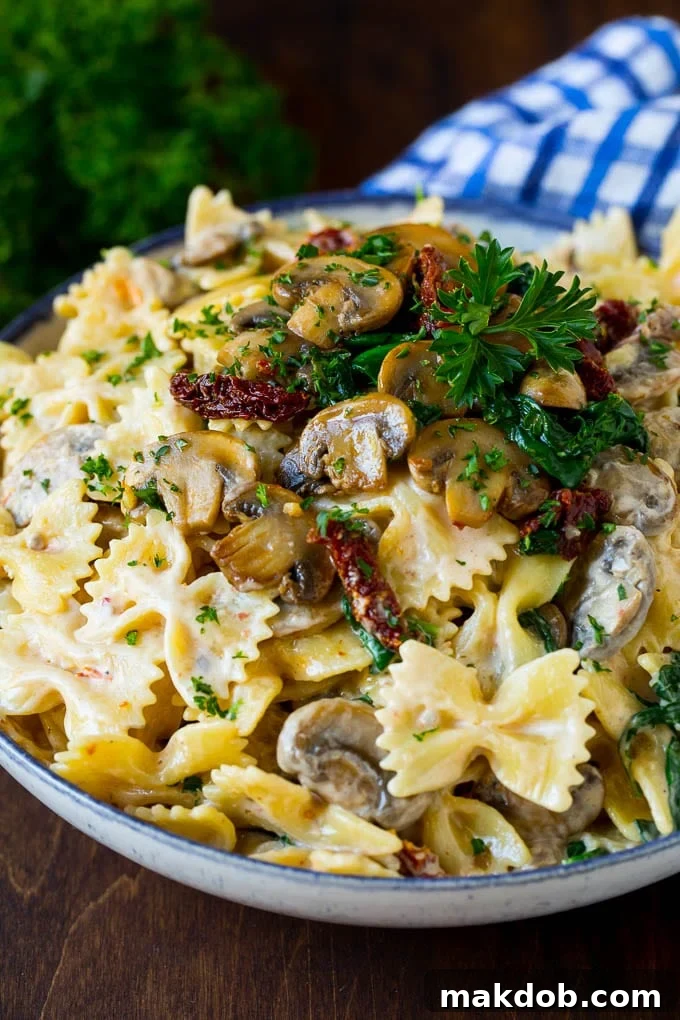 A beautifully plated bowl of creamy farfalle pasta, adorned with mushrooms and sun-dried tomatoes.