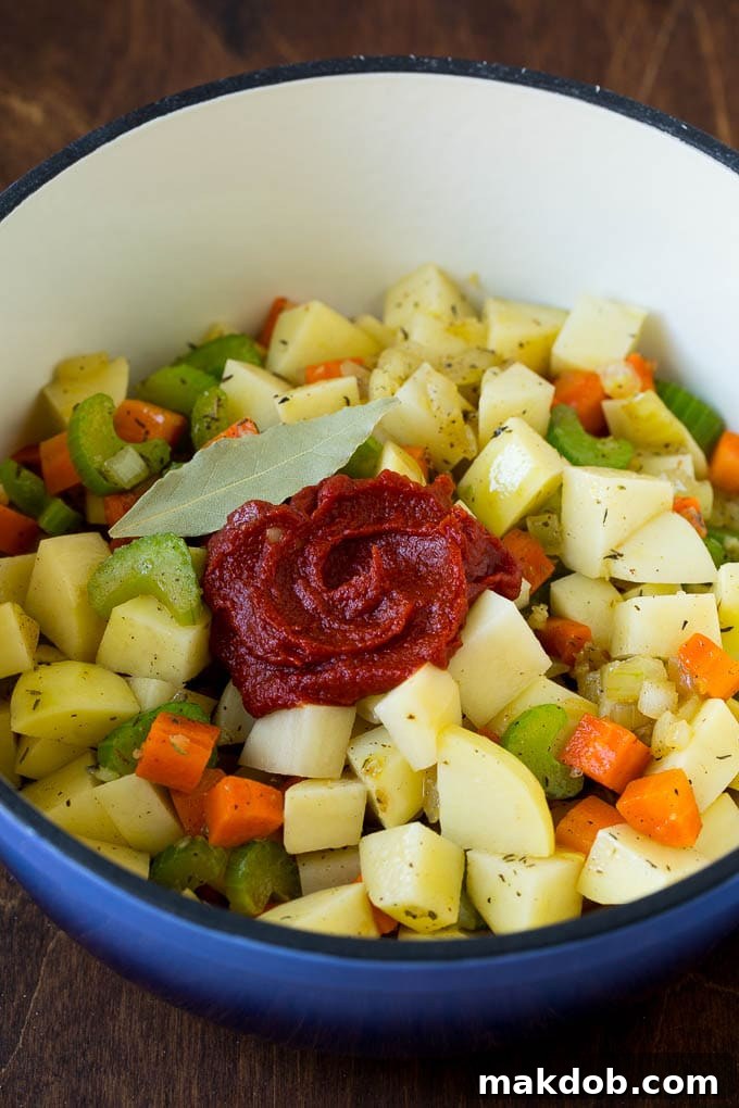 Potatoes, vegetables, herbs, and tomato paste ready to be cooked in a soup pot.