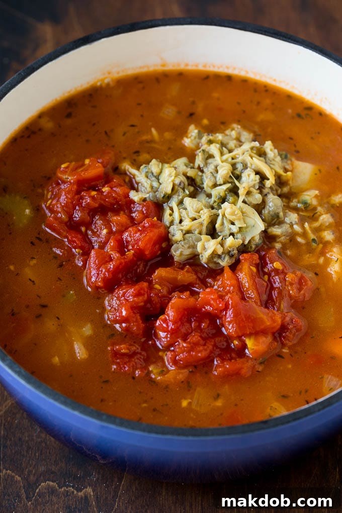 A pot of red clam chowder broth topped with diced tomatoes and baby clams.