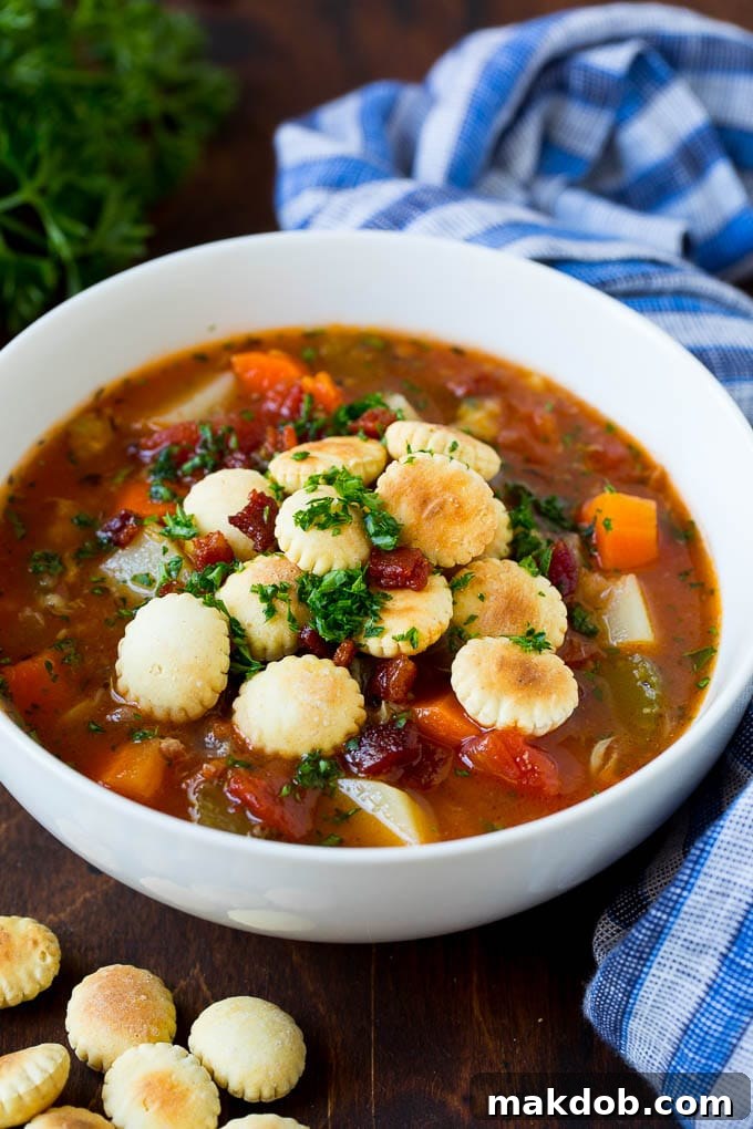 A bowl of Manhattan clam chowder topped with oyster crackers, crispy bacon, and fresh parsley.