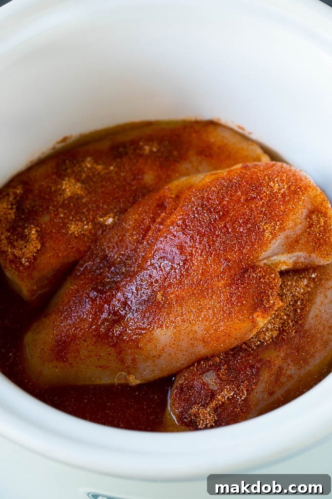 A slow cooker filled with seasoned chicken breasts and chicken broth, simmering to perfection.