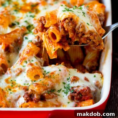 A spoon serving up a portion of baked rigatoni pasta.