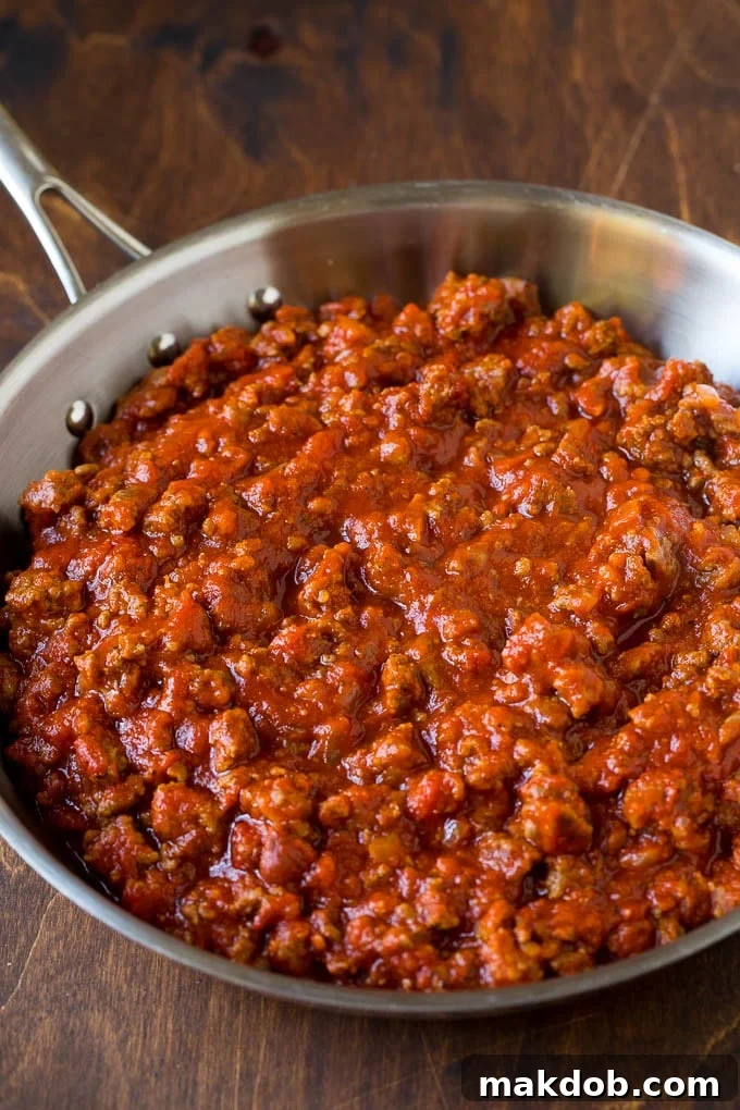 Homemade meat sauce simmering in a large pan, rich with tomatoes, ground beef, and Italian sausage.