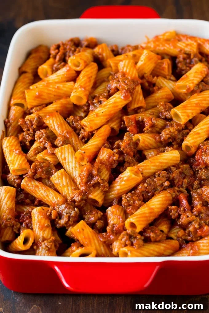 Rigatoni pasta perfectly tossed with a rich, red meat sauce in a large pan, ready for assembly.