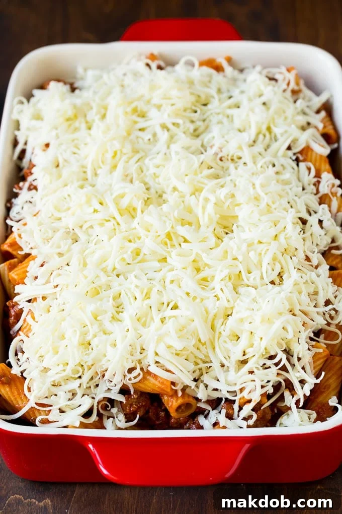 A baking pan filled with rigatoni pasta and meat sauce, topped generously with shredded mozzarella cheese, ready for the oven.