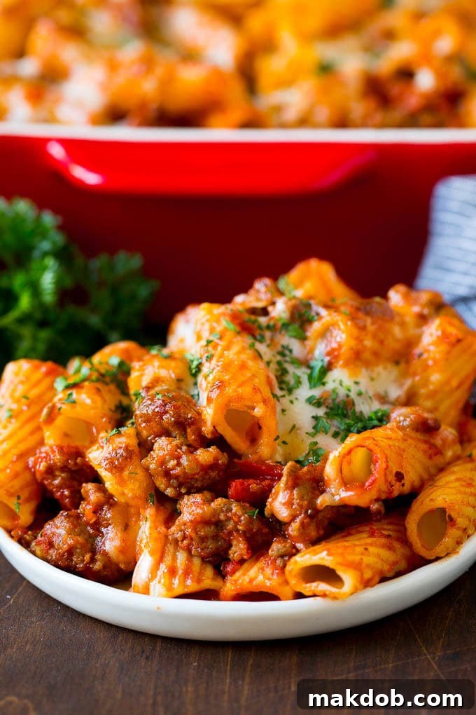A plate of baked rigatoni pasta, beautifully topped with melted, browned cheese and garnished with fresh parsley.