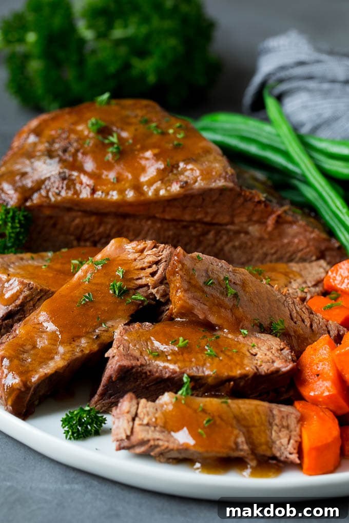 Slow cooker brisket sliced and topped with sauce, served with vegetables.