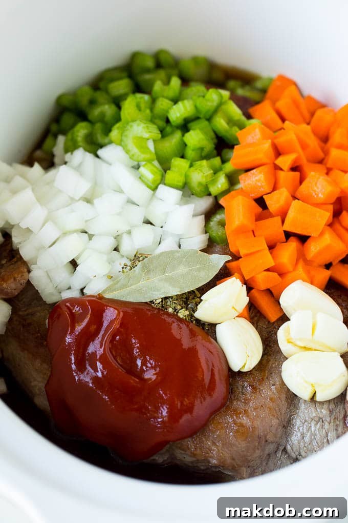 Slow Cooker Brisket Recipe | Crockpot Brisket #beef #slowcooker #crockpot #dinner #dinneratthezoo Brisket, vegetables, herbs, and seasonings arranged within a slow cooker before cooking.