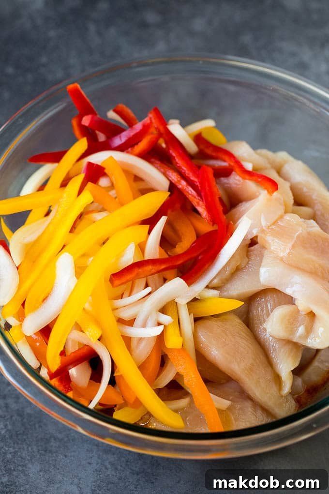 Chicken breasts and peppers in a bowl of marinade.