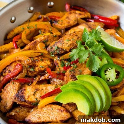 A pan of chicken fajitas with peppers and onions, topped with sliced avocado and cilantro.