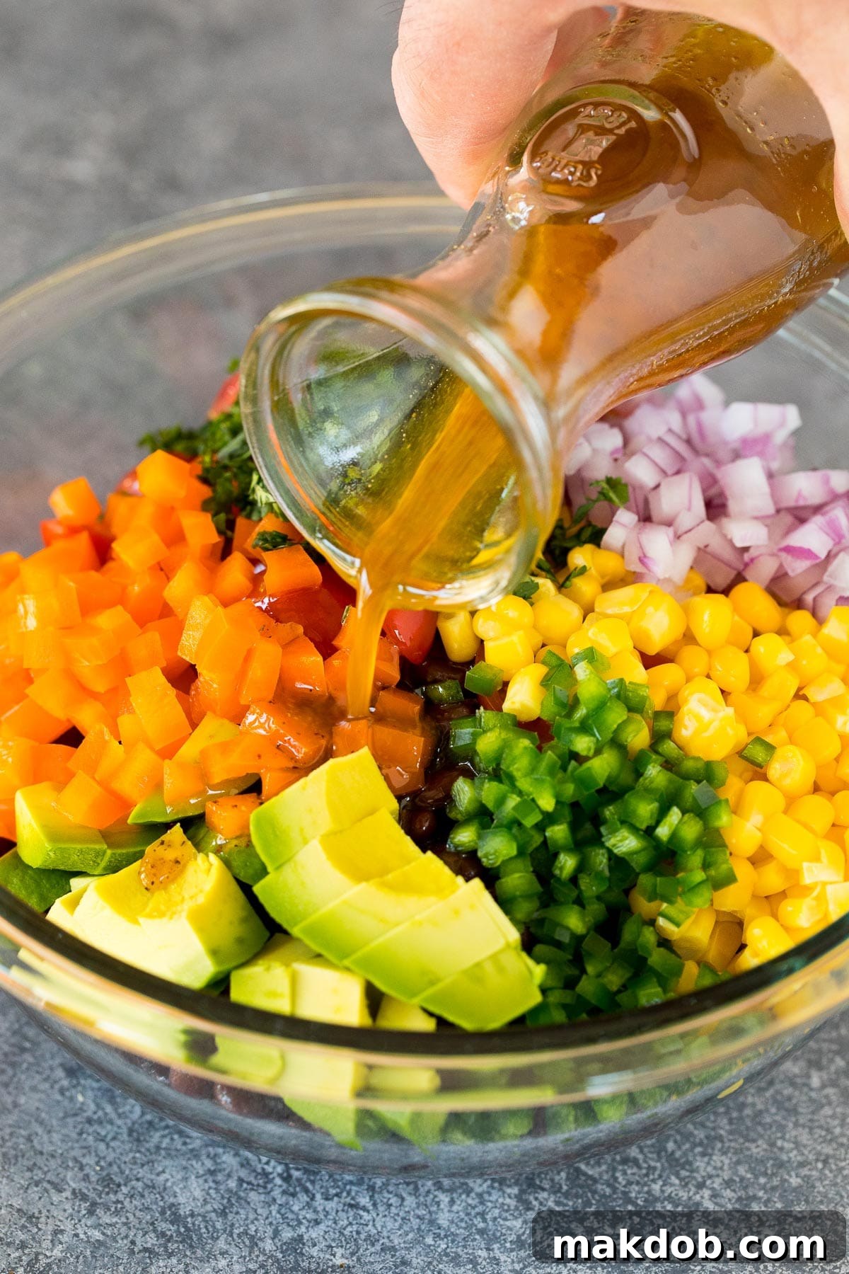 Southwestern Black Bean Medley 6 Zesty lime dressing being poured over a colorful black bean and vegetable salad in a large bowl.