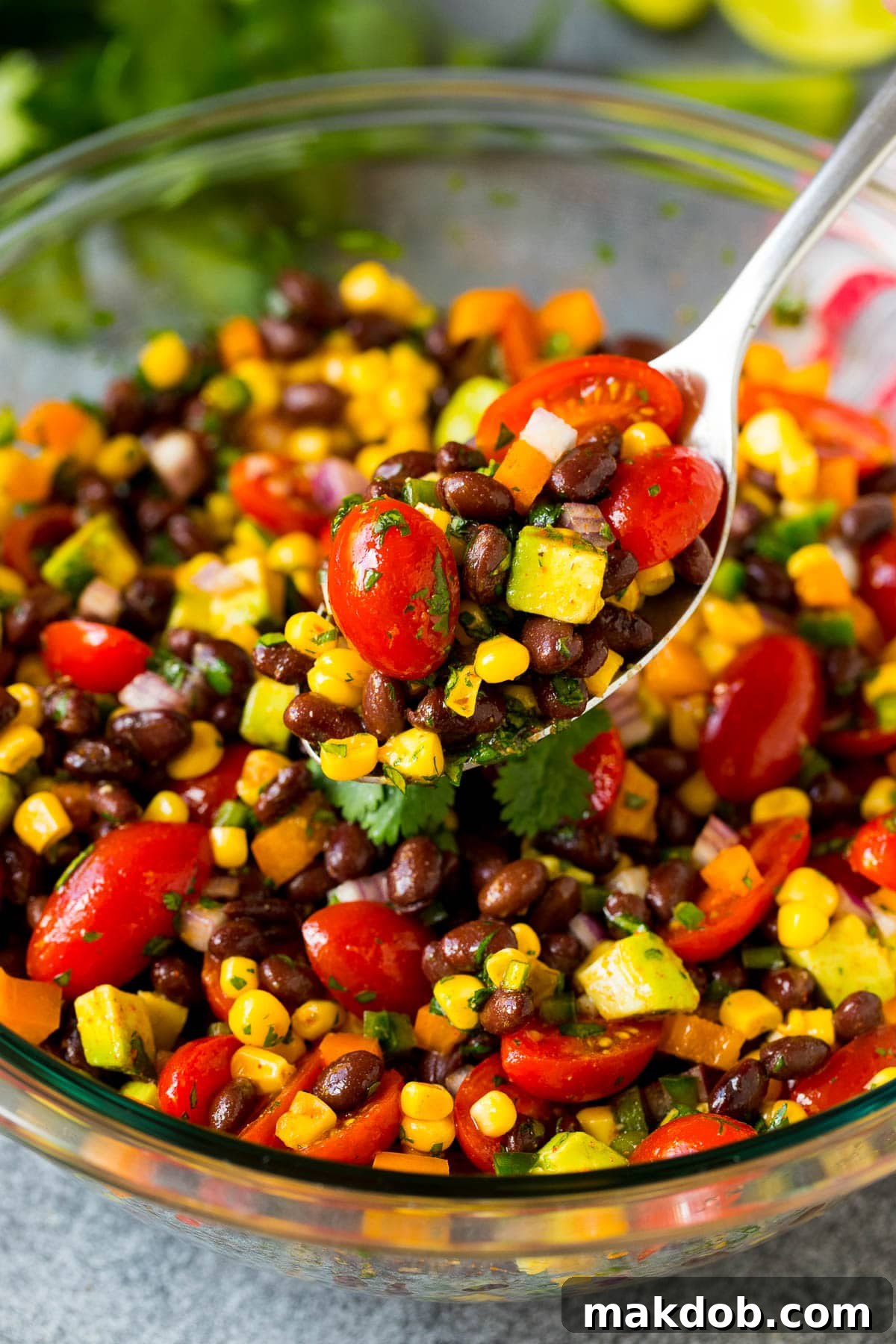 Southwestern Black Bean Medley 7 A serving spoon lifting a scoop of vibrant black bean salad, highlighting the mix of beans, corn, peppers, and avocado.