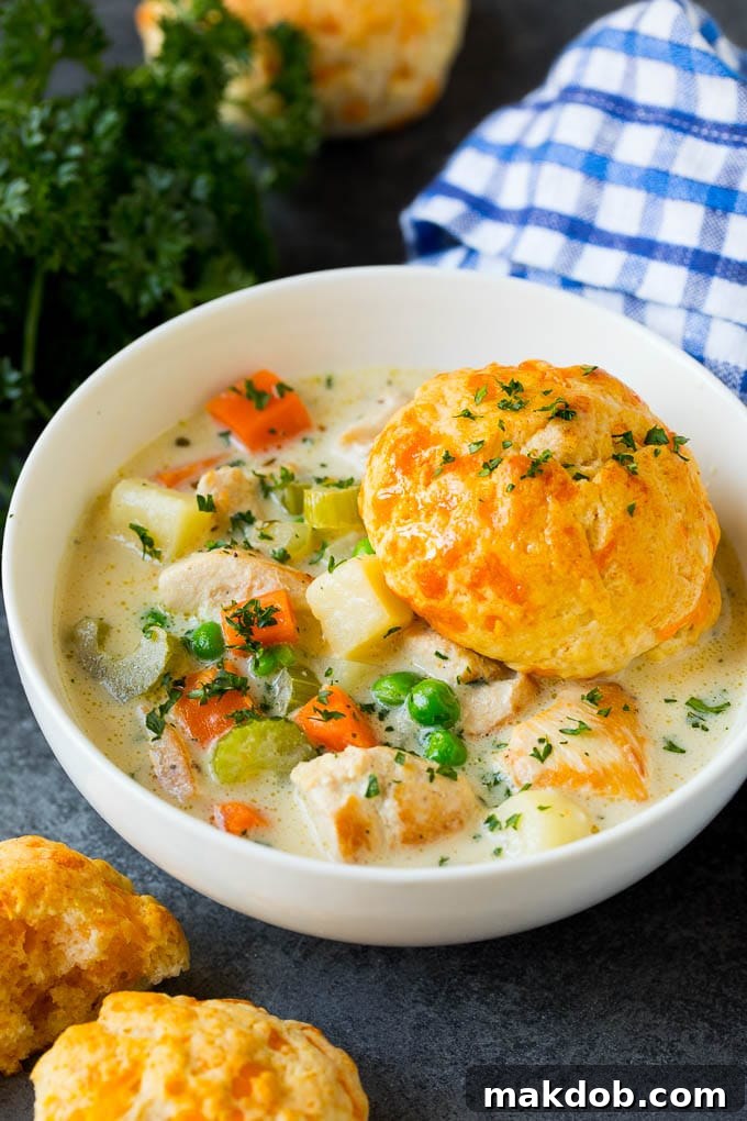 Classic Chicken Pot Pie Soup Recipe with Cheddar Biscuits | Ultimate Comfort Food A steaming bowl of creamy chicken pot pie soup, generously topped with a golden-brown homemade cheddar biscuit, ready to be enjoyed.