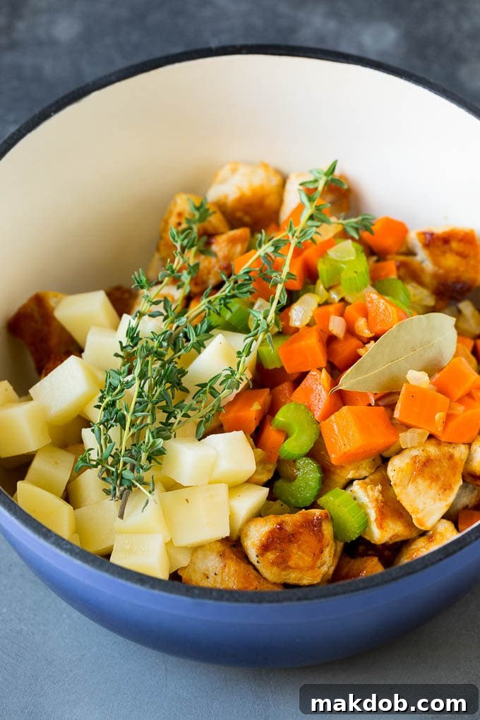 Simmering Chicken Pot Pie Soup Base with Fresh Ingredients A large soup pot filled with a rich mixture of chicken broth, diced vegetables, and potatoes, simmering on the stovetop.