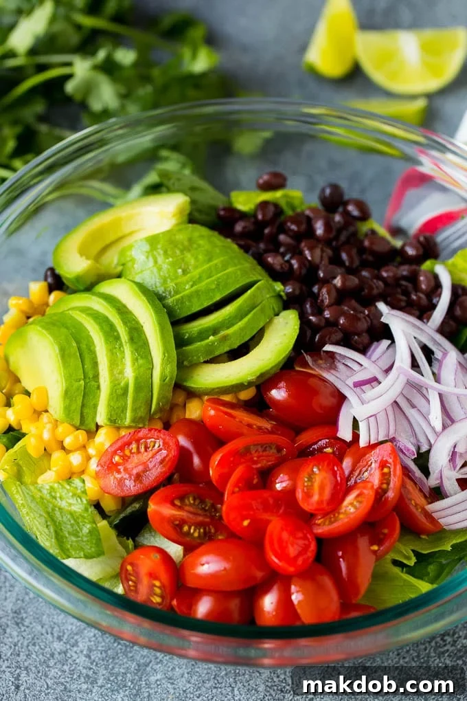 Lettuce, tomatoes, onion, corn, avocado and black beans in a bowl.