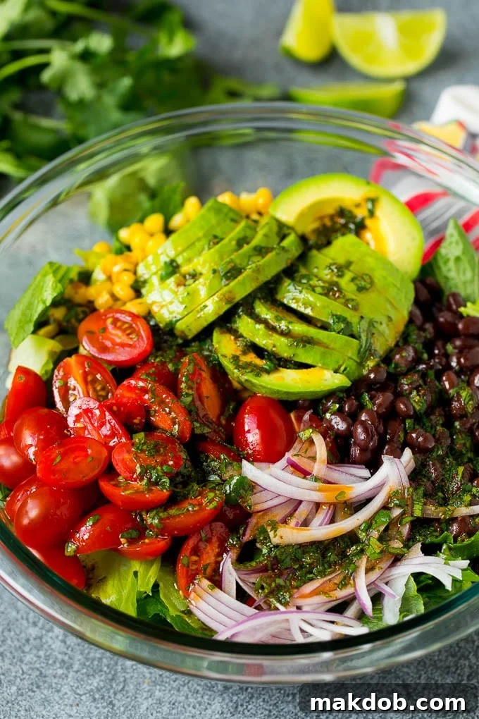 Zesty lime dressing being drizzled over a colorful bowl of lettuce, tomatoes, avocado, and black beans for a Mexican salad.