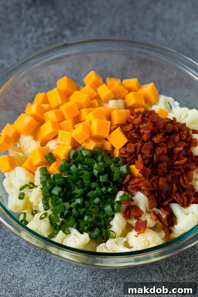 A bowl of cauliflower with bacon, cheese and green onions on top, ready for dressing.