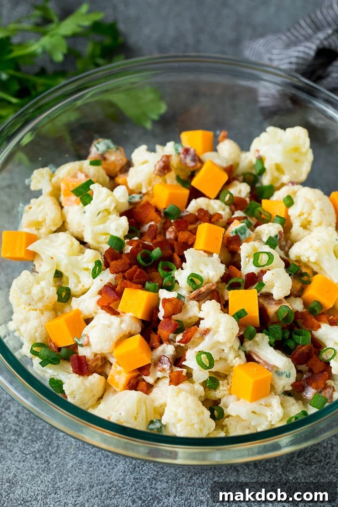 A bowl of cauliflower salad garnished with bacon and green onions, ready to serve.