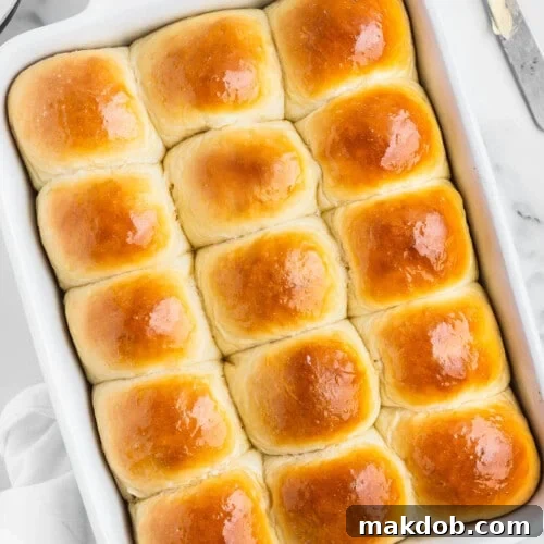 A pan of homemade dinner rolls with melted butter and a knife on the side, highlighting their golden-brown crust and soft texture, ready to be served.