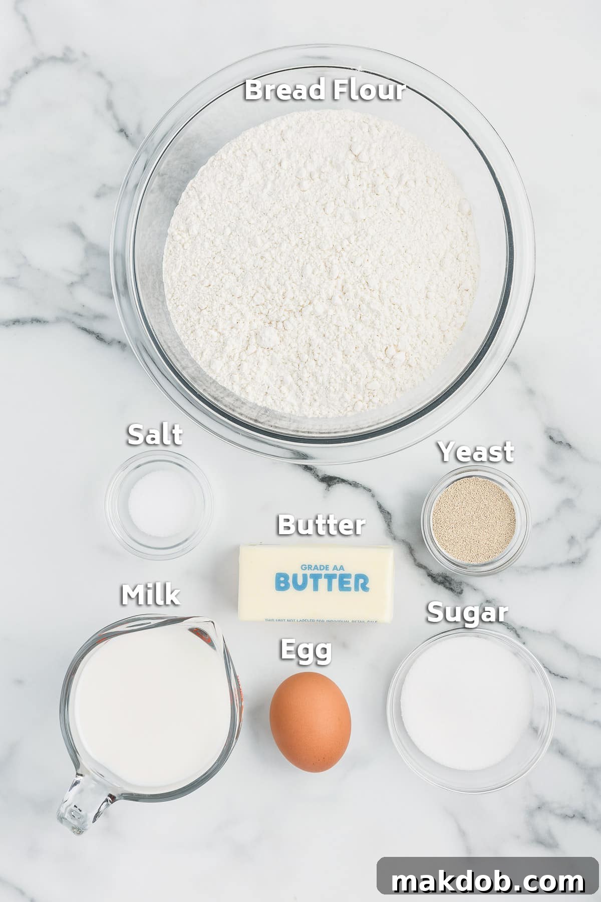 A selection of essential ingredients laid out, including flour, granulated sugar, a cracked egg, a bowl of instant yeast, and a carton of milk, ready for making homemade dinner rolls.